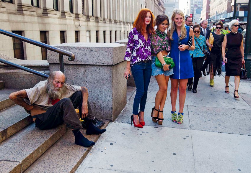 Fashionistas pose for photographs in front of a homeless man outside Moynihan Station following a showing of the Rag & Bone Spring/Summer 2013 collection during New York Fashion Week